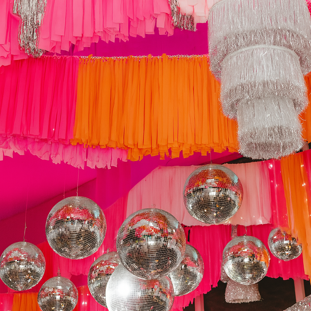 Decorative ceiling with colorful streamers and disco balls against a pink and orange background