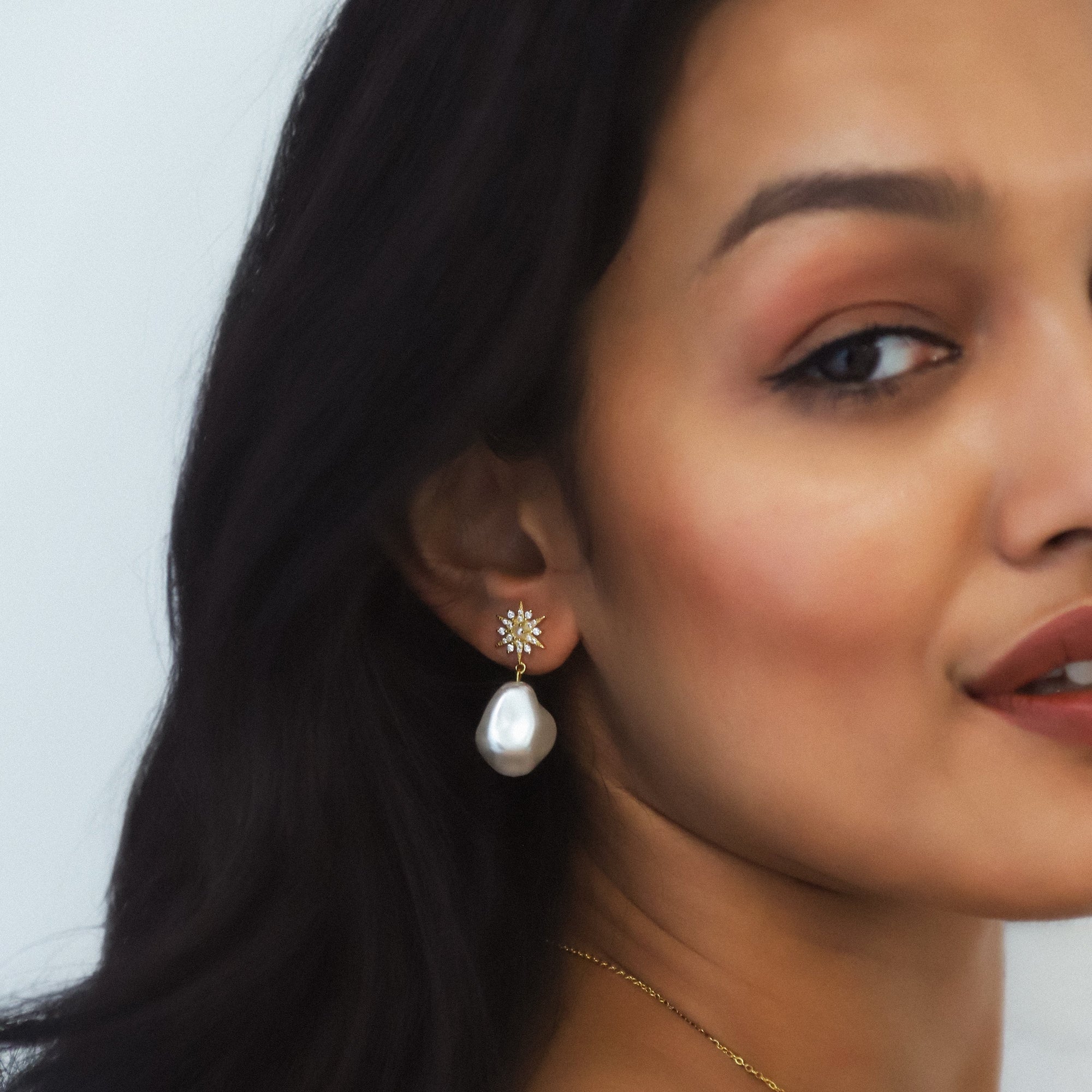 Close-up of a woman wearing pearl earrings with a neutral background