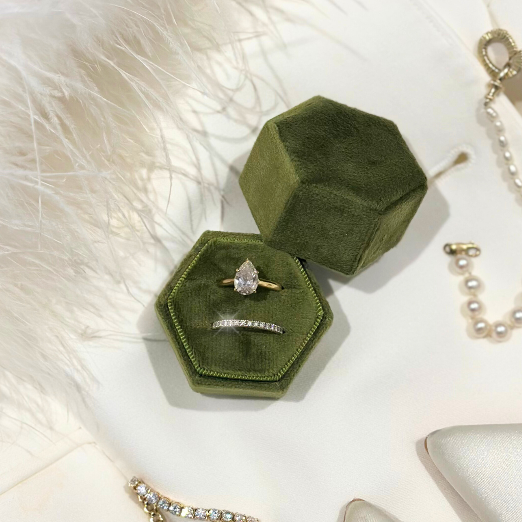 Green hexagonal velvet jewelry box with a ring on a white fur surface