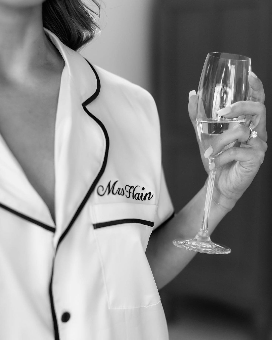 Person wearing a white outfit with 'Mrs Flain' text, holding a wine glass.
